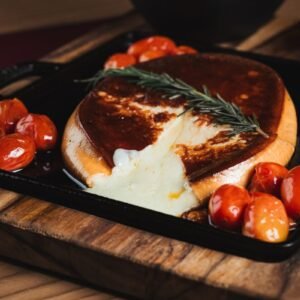 Melted provolone cheese paired with grilled cherry tomatoes on a wooden board for a savory appetizer.