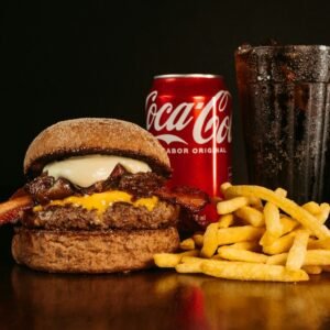 a hamburger with bacon, cheese and fries next to a coke